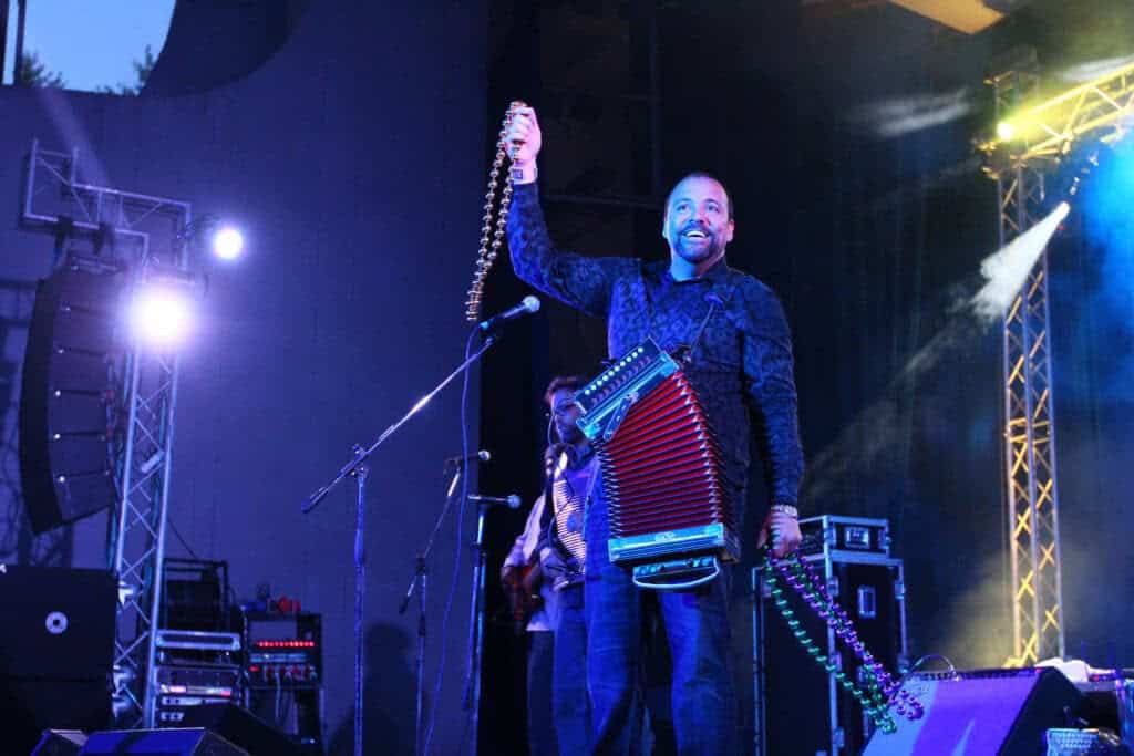 Smiling man holds microphone, has accordion strapped around his chest.